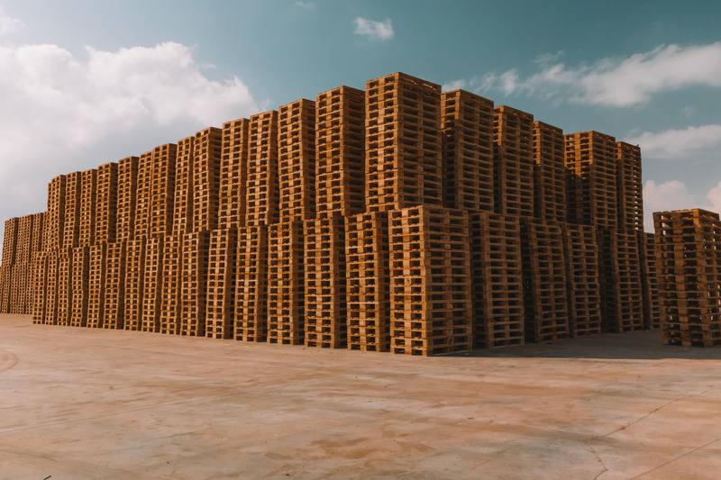 A big block of stacked wooden pallets in an open yard under a blue sky
